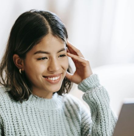 Hispanic woman working remotely on laptop near notepad in apartment